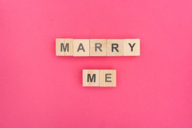 top view of marry me lettering made of wooden cubes on pink background clipart