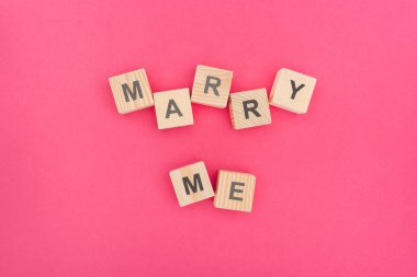 top view of marry me lettering made of wooden blocks on pink background