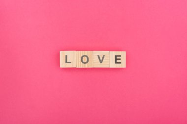 top view of love lettering made of wooden blocks on pink background clipart