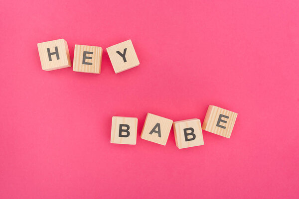 top view of hey babe lettering made of wooden blocks on pink background