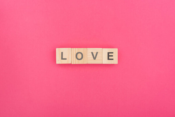 top view of love lettering made of wooden blocks on pink background