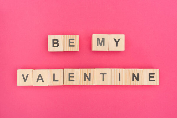 top view of be my valentine lettering made of wooden cubes on pink background