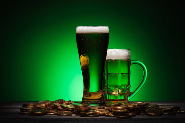 glasses of beer standing on wooden table on st patricks day on green background