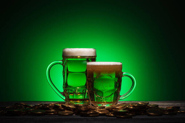 glasses of beer standing near golden coins on green background