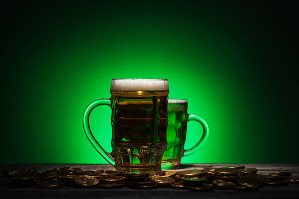 glasses of irish beer standing near golden coins on green background
