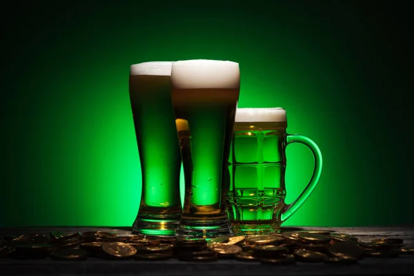 glasses of irish beer standing near golden coins on table on green background