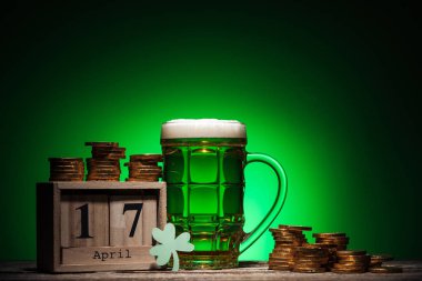 glass of green irish beer near golden coins and cube calendar on green background clipart