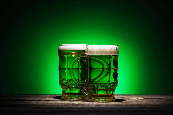 glasses of irish beer standing on wooden table on green background