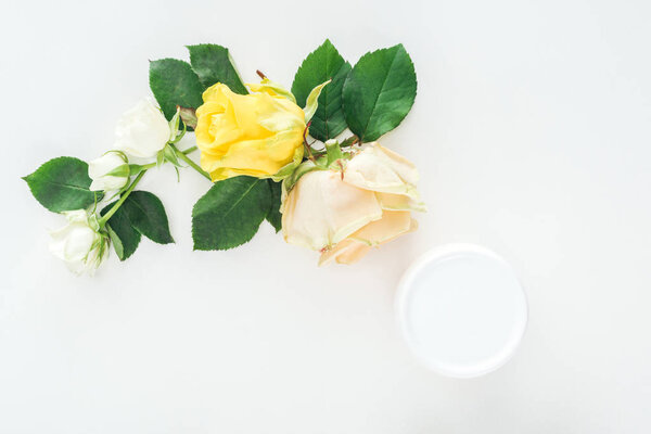 top view of composition with roses and beauty cream in bottle on white background