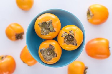 selective focus of whole orange persimmons on blue glass plate clipart