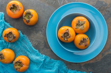 top view of whole and ripe persimmons in blue plates  clipart