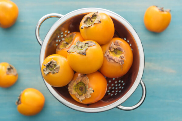 селективный фокус целых и спелых хурм в дуршлаге на синем фоне
 