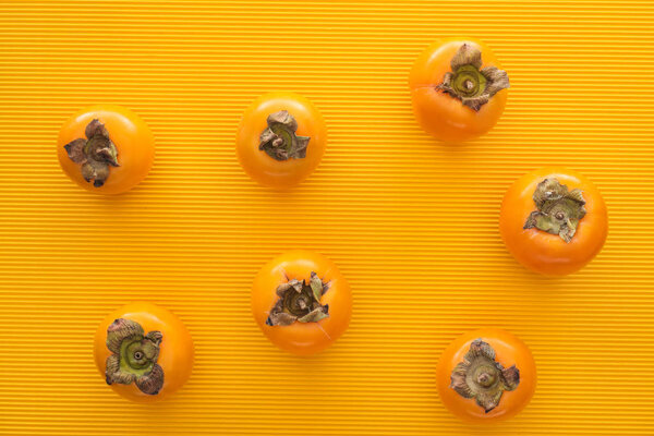 top view of whole orange persimmons on yellow background 