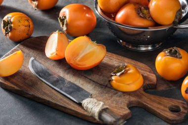 dilimlenmiş ve bütün turuncu persimmons kesme tahtası ve kevgir 