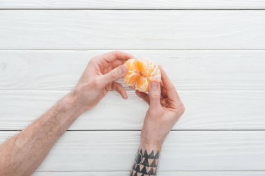 dövmeli adam soyulmuş mandalina Beyaz ahşap yüzeyde tutan görünümünü kırpılmış