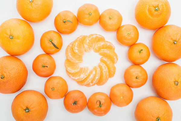 flat lay with circles of peeled tangerine slices and whole tangerines on white background