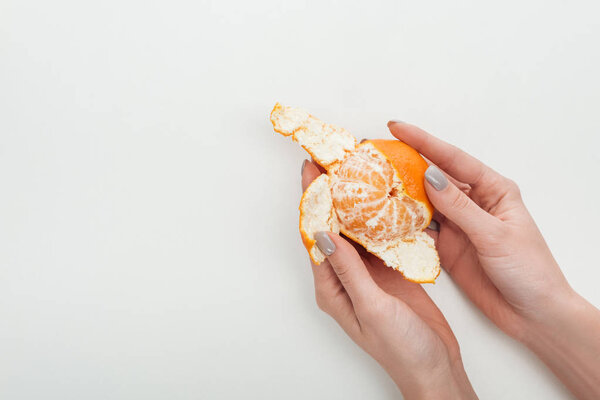 cropped view of woman peeling ripe orange tangerine on white background