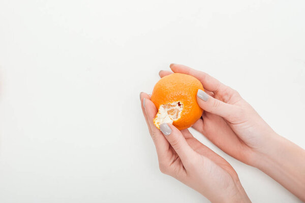 partial view of woman peeling ripe orange tangerine on white background