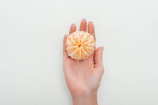 partial view of woman holding peeled whole tangerine in palm on white background