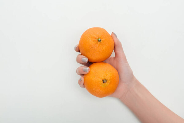 cropped view of woman holding two whole tangerines in hand on white background