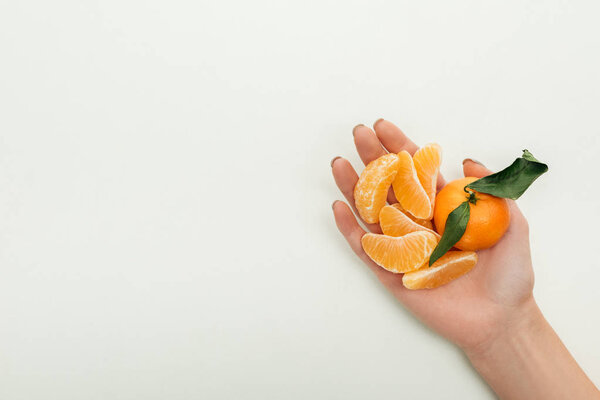 partial view of woman holding peeled tangerine slices and whole tangerine on white background