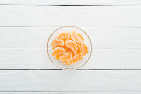 top view of peeled tangerine slices in glass bowl on wooden white background