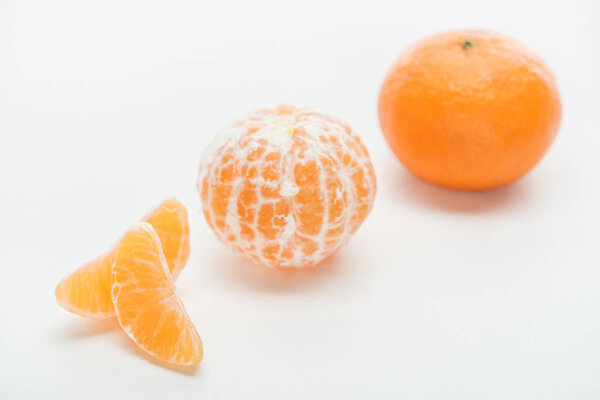 selective focus of ripe orange whole peeled and unpeeled tangerines with slices on white background