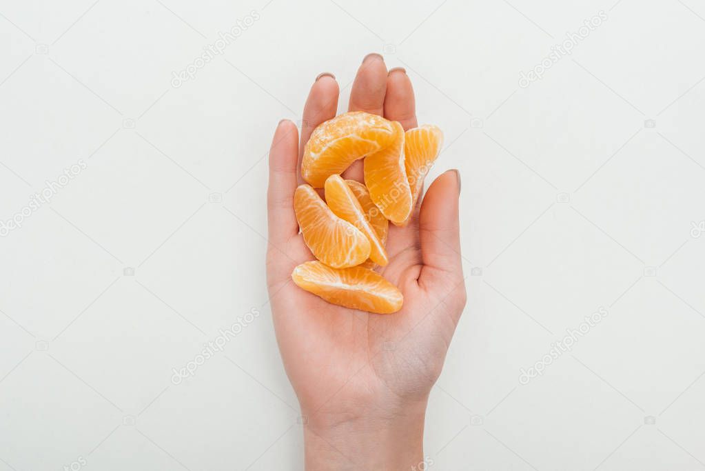 partial view of woman holding peeled tangerine slices on white background