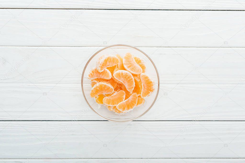 top view of peeled tangerine slices in glass bowl on wooden white background