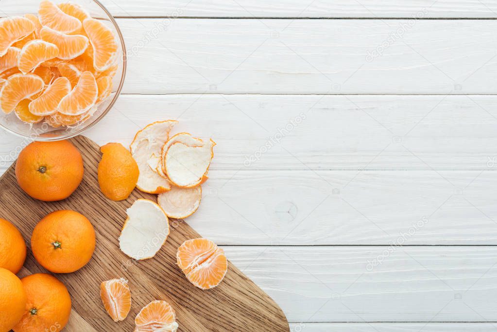 top view of peeled tangerines on wooden cutting board on white wooden table