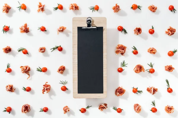 top view of empty clipboard with cherry tomatoes, leaves and prosciutto