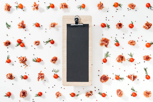 top view of blank clipboard with cherry tomatoes, leaves, spices and prosciutto