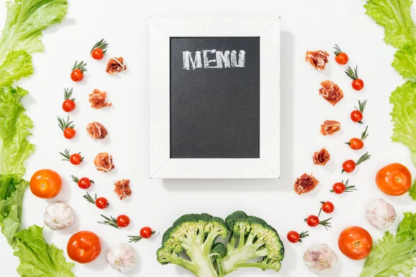 Top view of chalk board with menu lettering among tomatoes, lettuce leaves, prosciutto, broccoli and garlic — Stock Image Top View Chalk Board Menu Lettering Tomatoes Lettuce Leaves Prosciutto Stock Image