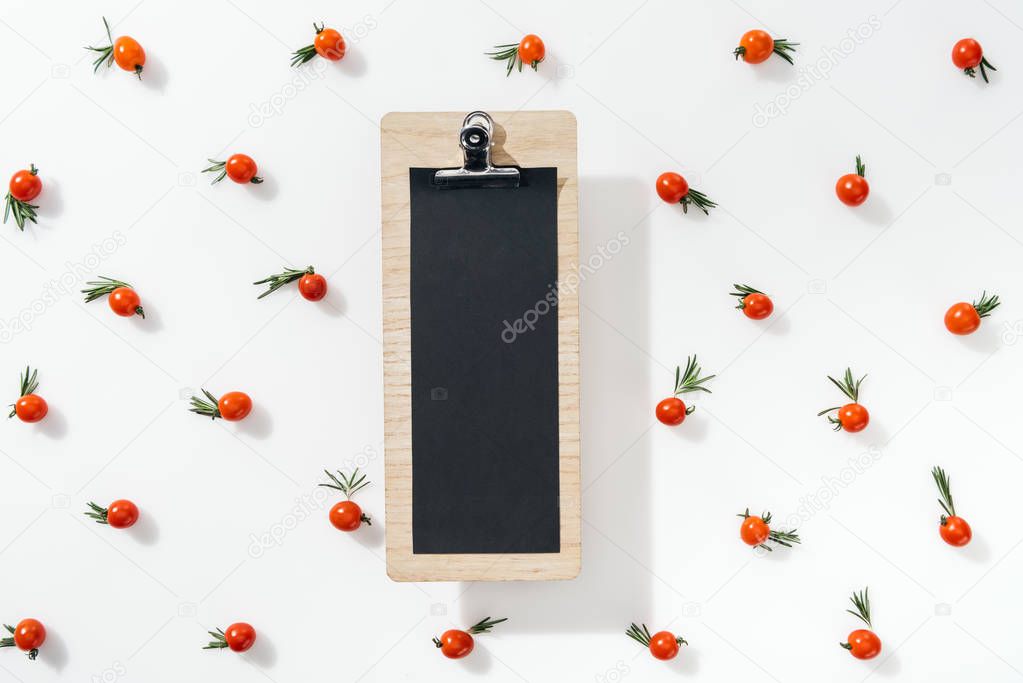 top view of empty clipboard with cherry tomatoes and leaves on white background 