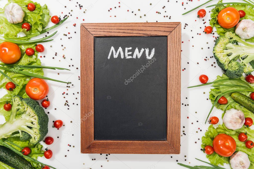 top view of chalk board with menu lettering among tomatoes, lettuce leaves, cucumbers, onion, spices and garlic