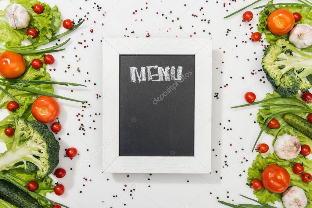 top view of chalk board with menu lettering among tomatoes, lettuce leaves, cucumbers, onion, spices and garlic