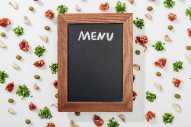 top view of chalk board with menu lettering among prosciutto, olives, garlic cloves and greenery clipart