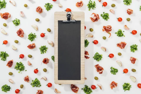 empty clipboard among prosciutto, olives, garlic cloves, greenery and cherry tomatoes