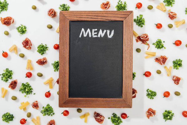 top view of chalk board with menu lettering among olives, prosciutto, greenery, cut cheese and cherry tomatoes