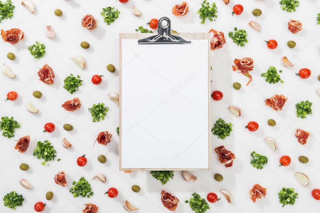 top view of empty clipboard among prosciutto, olives, garlic cloves, greenery and cherry tomatoes
