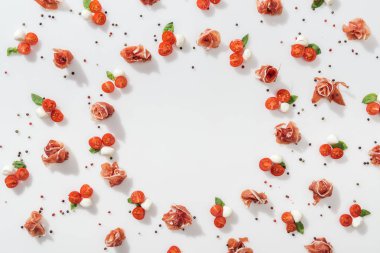 prosciutto kırmızı kiraz domates, mozzarella peyniri, yeşil fesleğen yaprakları ve beyaz zemin üzerine karabiber yakın düz lay