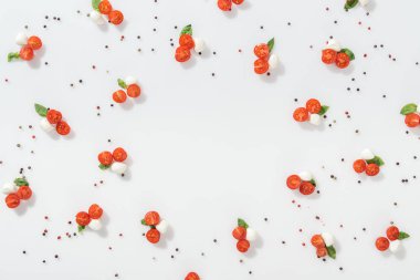 Kırmızı kiraz domates, mozzarella peyniri, yeşil fesleğen yaprakları ve beyaz zemin üzerine karabiber, düz lay