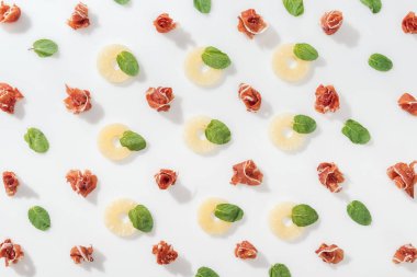 Yeşil fesleğen yaprakları ve beyaz arka plan üzerinde ananas yüzük yakınındaki lezzetli prosciutto düz lay