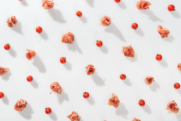 top view of tasty prosciutto near red cherry tomatoes on white background