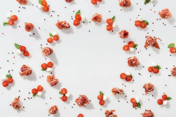 prosciutto kırmızı kiraz domates, mozzarella peyniri, yeşil fesleğen yaprakları ve beyaz zemin üzerine karabiber yakın düz lay