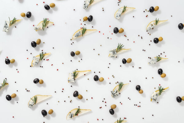 flat lay of sliced pears with blue cheese and rosemary twigs near black and green olives on white background