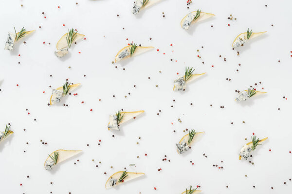 top view of sliced pears with blue cheese and rosemary twigs near black and red peppercorns isolated on white 