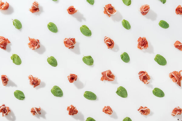 top view of delicious prosciutto near green basil leaves on white background