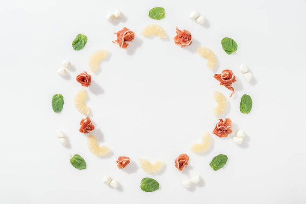 flat lay of delicious prosciutto near green basil leaves, sliced pineapples and  mozzarella cheese on white background