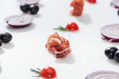 selective focus of tasty prosciutto near cherry tomatoes with rosemary twigs near red onion rings and black olives on white background clipart